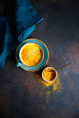 Top down view of turmeric latte cup on a textured dark background.