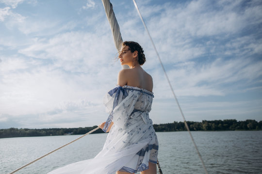 ?oung girl stands on a yacht with white sails in a flying dress.