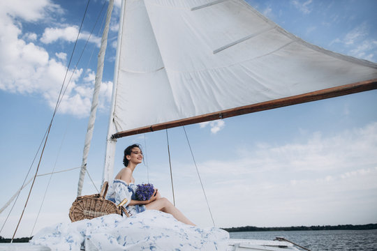 Нoung girl stands on a yacht with white sails in a flying dress.