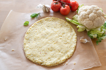 raw pizza base from shredded cauliflower on baking paper, healthy vegetable alternative for low...