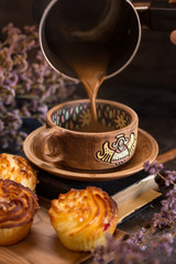 Nearby lies a fresh cheesecake. Handmade pottery with painting. Around there are many small lilac flowers. Pleasant romantic mood.