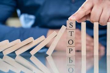 Businessperson's Finger Stopping Falling Dominoes