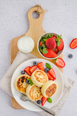 Fried cottage cheese pancakes or syrniki with fresh berries on a white plate with sour cream. Gluten free. Traditional breakfast of Ukrainian and Russian cuisine. Vertical, top view.
