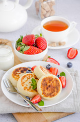 Fototapeta na wymiar Fried cottage cheese pancakes or syrniki with fresh berries on a white plate with sour cream. Gluten free. Traditional breakfast of Ukrainian and Russian cuisine. Vertical