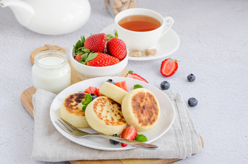 Fototapeta na wymiar Fried cottage cheese pancakes or syrniki with fresh berries on a white plate with sour cream. Gluten free. Traditional breakfast of Ukrainian and Russian cuisine. Horizontal.