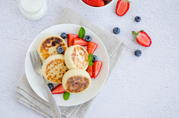 Fried cottage cheese pancakes or syrniki with fresh berries on a white plate with sour cream. Gluten free. Traditional breakfast of Ukrainian and Russian cuisine. Horizontal, top view.
