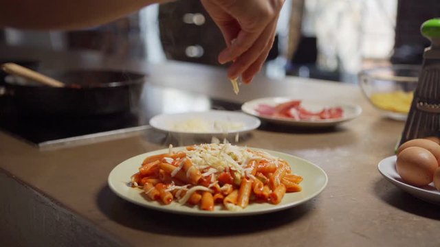Closeup hand of Italian restaurant chef pouring grated cheese on hot freshly made pasta with tomato sauce in slow motion