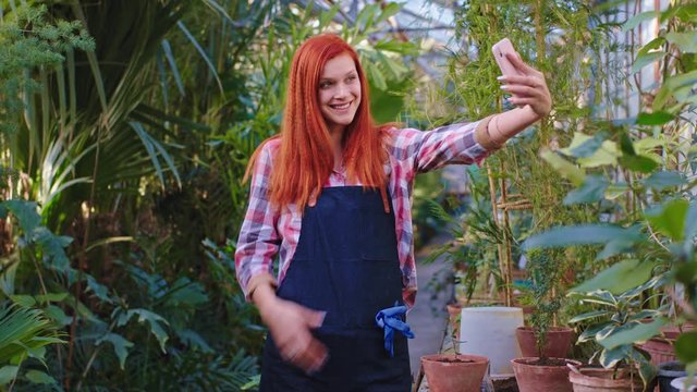 Great looking gardener redhead lady with a large smile she take some pictures with her smartphone in the middle of a greenhouse