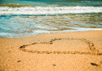 close-up image of a heart in the sand and azure sea wave in the background