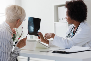 A female doctor sits at her desk and talks to a female patient while looking at her mammogram....