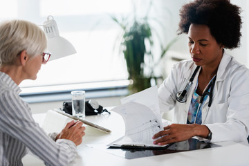 A female doctor sits at her office and examining elderly female patient
