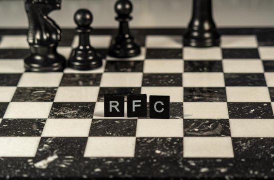 The acronym rfc for Request for Comments concept represented by black and white letter tiles on a marble chessboard with chess pieces