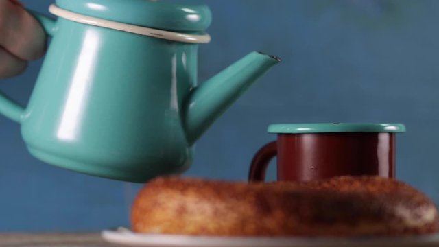 Pouring turkish tea into the cup with teapot and turkish simit is at background