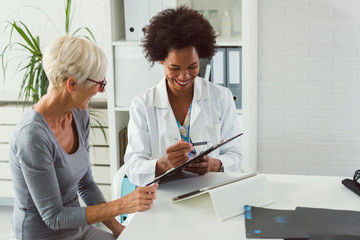 A female doctor sits at her desk and chats to an elderly female patient while looking at her  test results