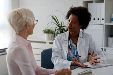 Fototapeta premium A female doctor sits at her desk and chats to an elderly female patient while looking at her test results