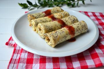 Traditional Russian and Ukrainian this pancakes with poppy seeds and strawberry jam on a white plate. National food for Maslenitsa.