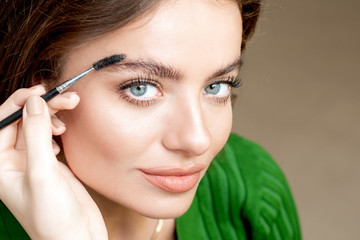 Obraz premium Closeup beautiful woman with eyebrow brush tool, makeup artist combs eyebrows close up.