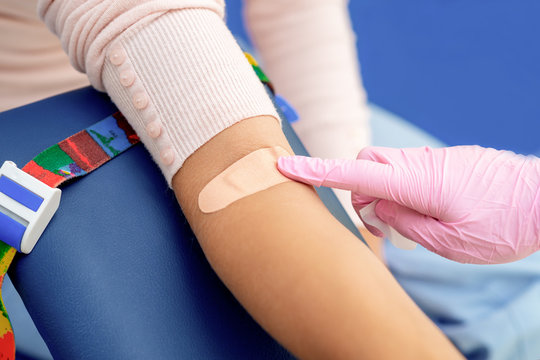 Doctor in rubber protective gloves putting an adhesive bandage on young woman's arm vein after blood test or injection of vaccine. Medical, pharmacy and healthcare concept.