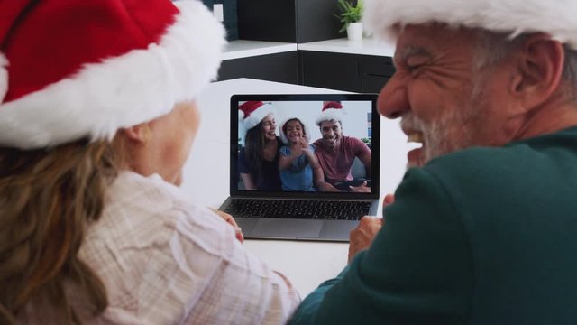 Multi-Generation Hispanic Family Wearing Santa Hats With Laptop Having Video Chat At Christmas