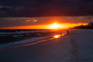 Colorful dark red sunset in Santa Rosa Beach with Pensacola coast in Florida Panhandle at Gulf of Mexico ocean waves with silhouette of people