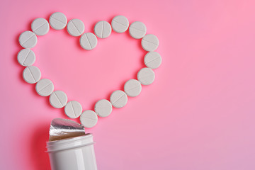 Heart pills and a bottle lie on a pink background. White pills on pink background. Medicine and healthy concept or mockup.