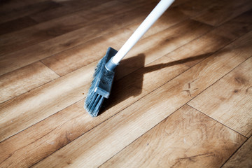 A broom consecrated by the sun rays sweeps dust from a wooden floor, parquet