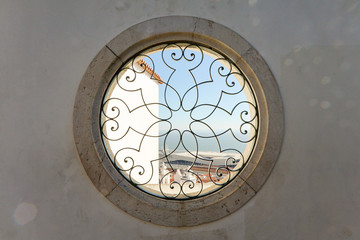 Round window with a black metal fence and a pattern in an old stone facade with a view to the sky