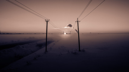 Winter dawn in the fields and electricity lines running forward.