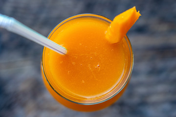 Freshly squeezed juice from mango in a glass goblet on the background wooden table, top view