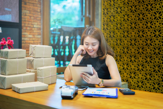Asian woman using smartphone or digital tablets chatting and checking stock product in warehouse. checks the number of items boxes store delivery to customers, Asian owner or small business concept.