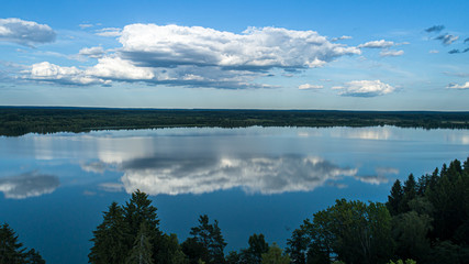 Cumulus clouds reflected in the mirror waters of a lake in sunny weather.