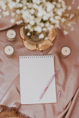 Notebook with pen on fabric background. Around a candle and a bouquet of flowers