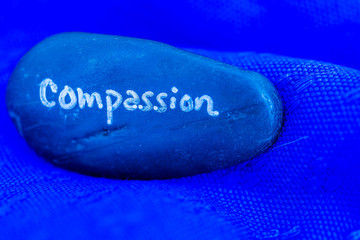 Compassion written on a stone. Bright blue tones and background