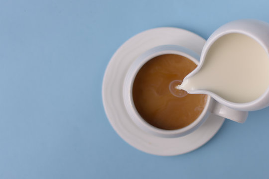Pouring milk from small ceramic pitcher into a cup of coffee