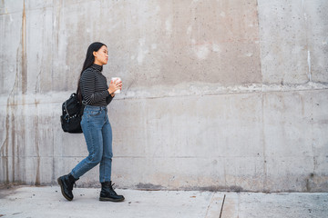 Asian woman walking and holding a cup of coffee.