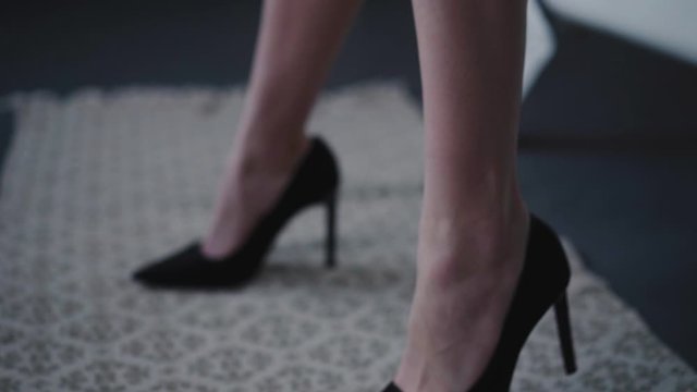 Unrecognizable female bare legs in black shoes posing at camera. Slowly