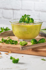 Ready to eat fresh hot broccoli puree soup with pieces of broccoli and parsley leaves in a bowl on a wooden table. Close-up. Healthy eating and lifestyle.