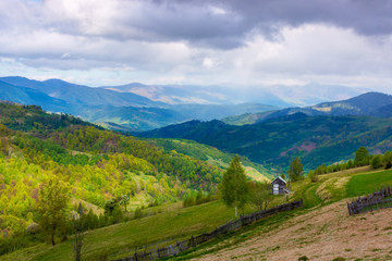 Fototapeta na wymiar rural landscape in mountains. dappeled light on forested hills. wooden fence along the hillside. beautiful nature scenery in spring. wonderful weather with clouds