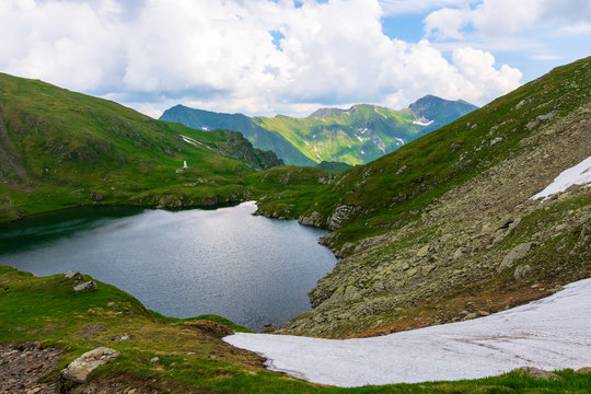 goat lake in the fagaras mountains of romania. popular travel destination. summer nature scenery with green grass and snow. ridge in the far distance beneath a cloudy sky