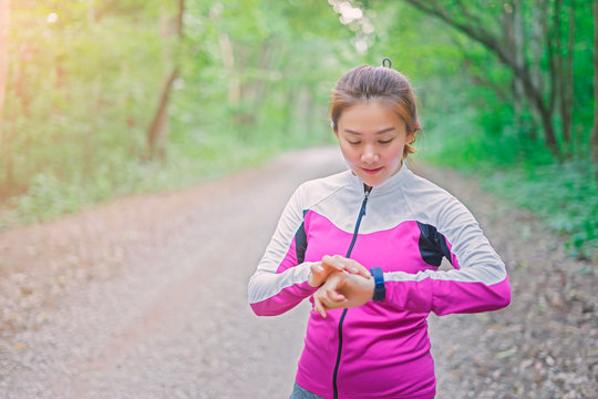 Asian Woman setting up the fitness smart watch for running. Sportswoman checking watch device,Forrest mountain road, exercise workout in nature road Autumn city forest park in fitness Sports concept