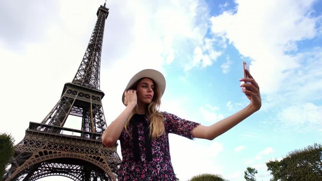 Millennial young girl taking selfie picture of Eiffel Tower on smartphone camera. Famous tourism & honeymoon landmark in Paris. 