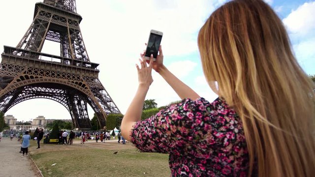 Millennial young girl taking picture of Eiffel Tower on smartphone camera. Famous tourism & honeymoon landmark in Paris. 