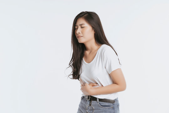 Asian woman unhappy looking sick, suffers from stomach ache stomachache isolated white background because of menstruation and eating spoiled food, Chronic gastritis. Abdomen bloating concept