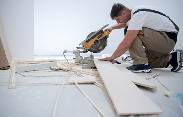 Man cutting laminate floor plank with electrical circular saw