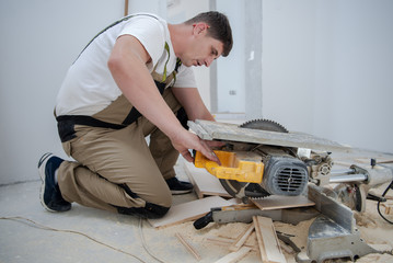 Man cutting laminate floor plank with electrical circular saw