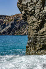 Mountain seascape. Vertical rock on which a wave rolls. Beach, recreation, tourism, travel.