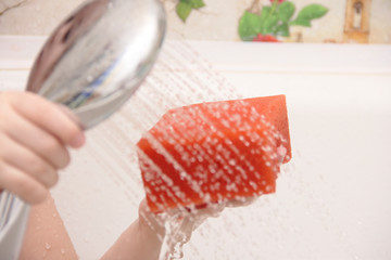 The little girl holds a shower in her hands and pours herself water.