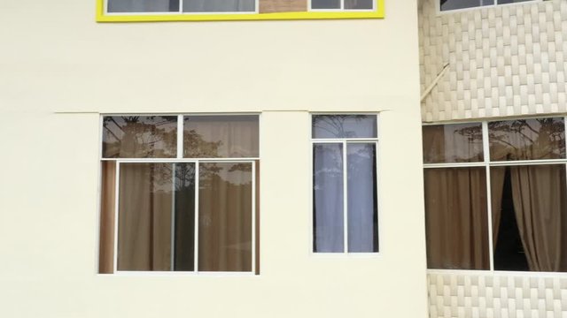 A moving view of a house with yellow walls and very diry windows with old curtains in front of the windows