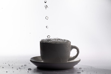 High speed studio photograph of water pouring and splashing into a white mug, isolated against a plain white background