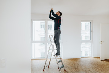 home owner standing on ladder fixing light installation - obrazy, fototapety, plakaty